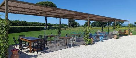 Un patio al aire libre con mesas y sillas, una pérgola y suelo de grava.