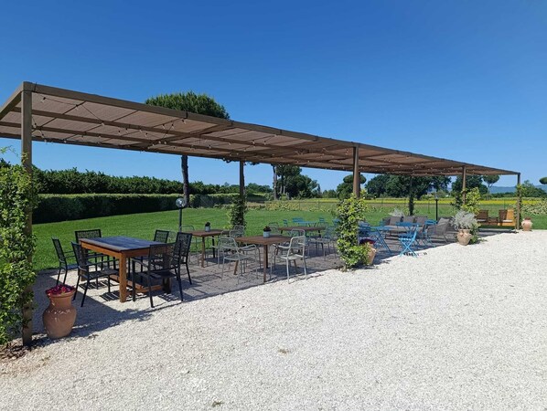 Une terrasse extérieure avec des tables et des chaises, une pergola et un sol en gravier.
