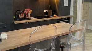 A modern kitchen with a wooden countertop, black cabinets, and a built-in oven. There are two pendant lights, a coffee machine, and a sign indicating Wi-Fi availability. - La Loge de l'Opéra – Elegant One-Bedroom Apartment in the Heart of the City (Toulon)