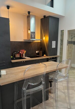 Eine moderne Küche mit Holzarbeitsplatte, schwarzen Schränken und einem eingebauten Ofen. Zwei Pendelleuchten, eine Kaffeemaschine und ein Schild, das WLAN anzeigt.