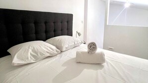 A modern hotel room with a large bed, white bedding, a black headboard, and a window with natural light. - La Loge de l'Opéra – Elegant One-Bedroom Apartment in the Heart of the City (Toulon)