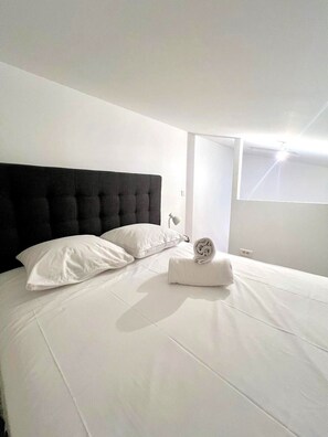 Ein modernes Hotelzimmer mit einem großen Bett, weißer Bettwäsche, einem schwarzen Kopfteil und einem Fenster mit Tageslicht.