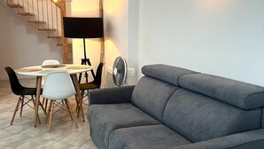 A modern living room with a grey sofa, a dining table with chairs, a standing lamp, and a staircase. - La Loge de l'Opéra – Elegant One-Bedroom Apartment in the Heart of the City (Toulon)