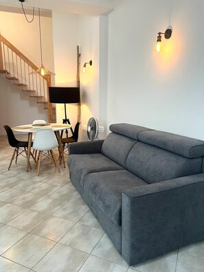 Ein modernes Wohnzimmer mit grauem Sofa, einem Esstisch mit Stühlen, einer Stehlampe und einer Treppe.