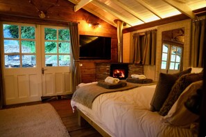 Une chambre confortable avec une cheminĂ©e en pierre, un lit, une tĂ©lĂ©vision et une vue sur lâextĂ©rieur.