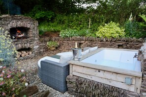 A stone fire pit, a hot tub, and a seating area in a garden setting.