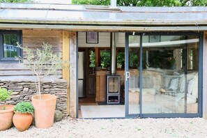 Une maison moderne avec une entrĂ©e dotĂ©e dâune porte en verre, un mur en pierre et un poĂȘle Ă bois.