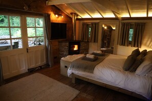 A bedroom with a stone fireplace, a bed with pillows, a window with curtains, and a door.