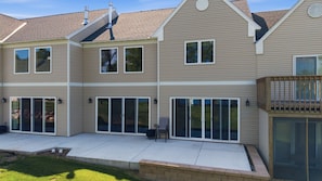A two-story house with a covered patio, large sliding glass doors, and a visible chimney. - NEW! Fairway Views, Near Mille Lacs, Private Deck (Onamia)