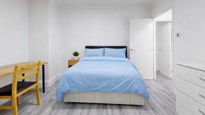 A bedroom with a bed, a desk, a chair, a nightstand with a plant, and a wardrobe. - Discover This Spacious Living Space Kings Cross (London)