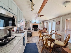 A modern kitchen with a microwave, stove, and sink. There is a dining area with wicker chairs and a glass table.