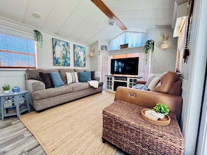 A living room with a brown sofa, a brown leather chair, a TV, and a large window with blinds.