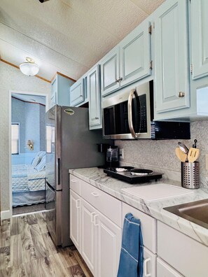 A kitchen with light blue cabinets, a stainless steel refrigerator, a microwave, and a coffee maker.