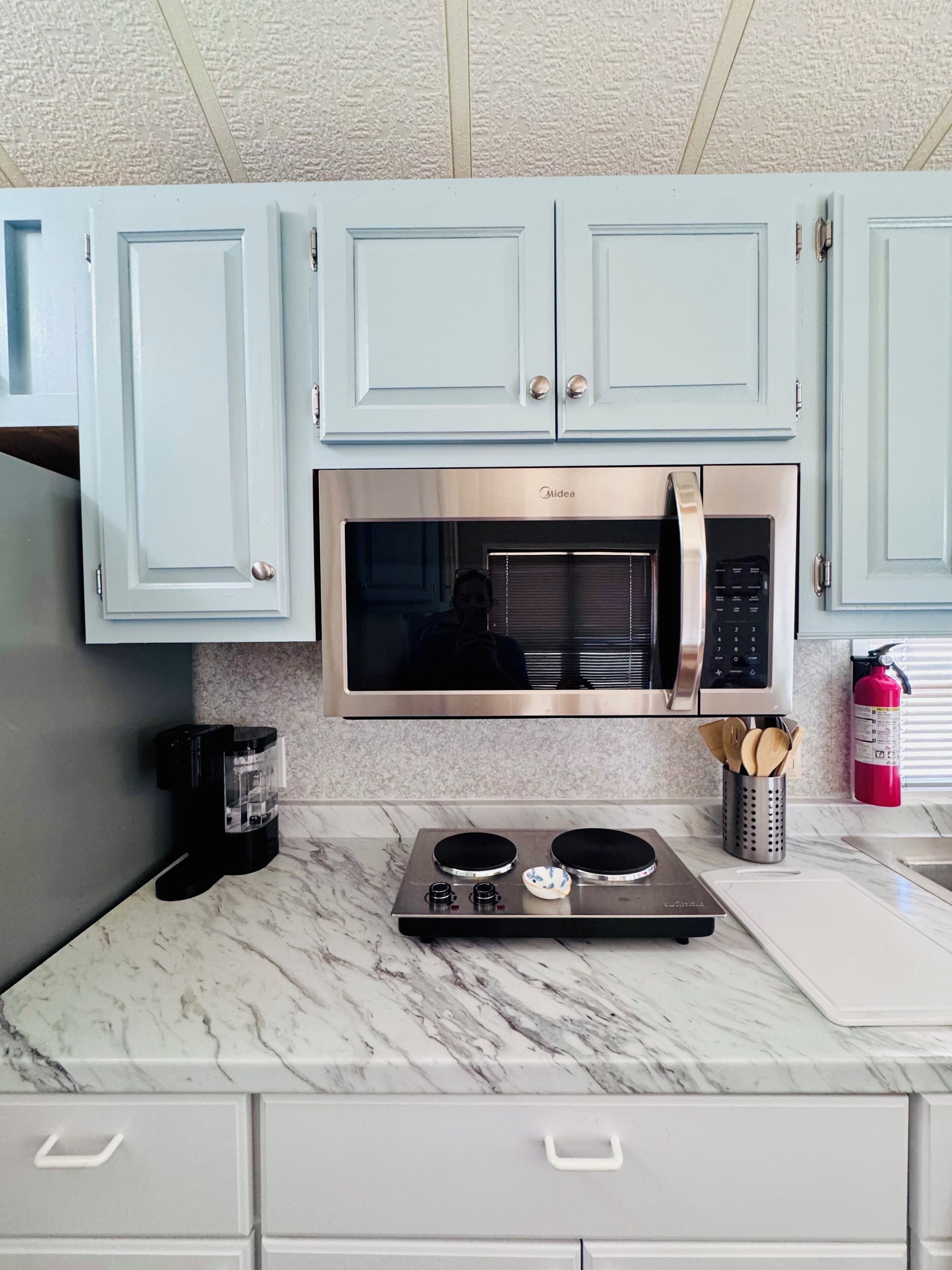 A kitchen with light blue cabinets, a stainless steel microwave, a gas stove, and a coffee maker.
