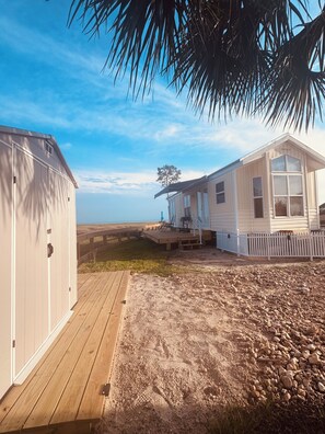 Une maison de plage dotée d’une terrasse en bois, d’une cour clôturée et offrant une vue dégagée sur la plage.