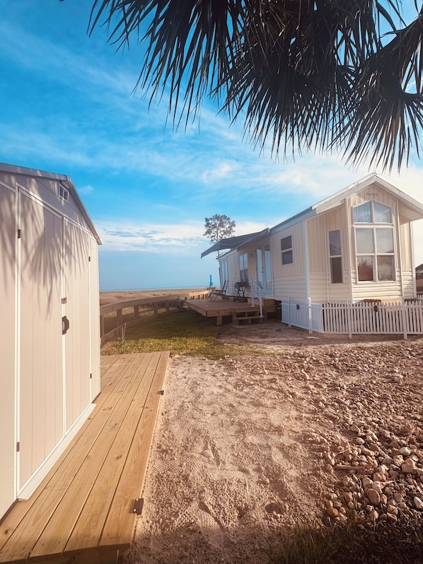 A beach house with a wooden deck, a fenced yard, and a clear view of the beach.