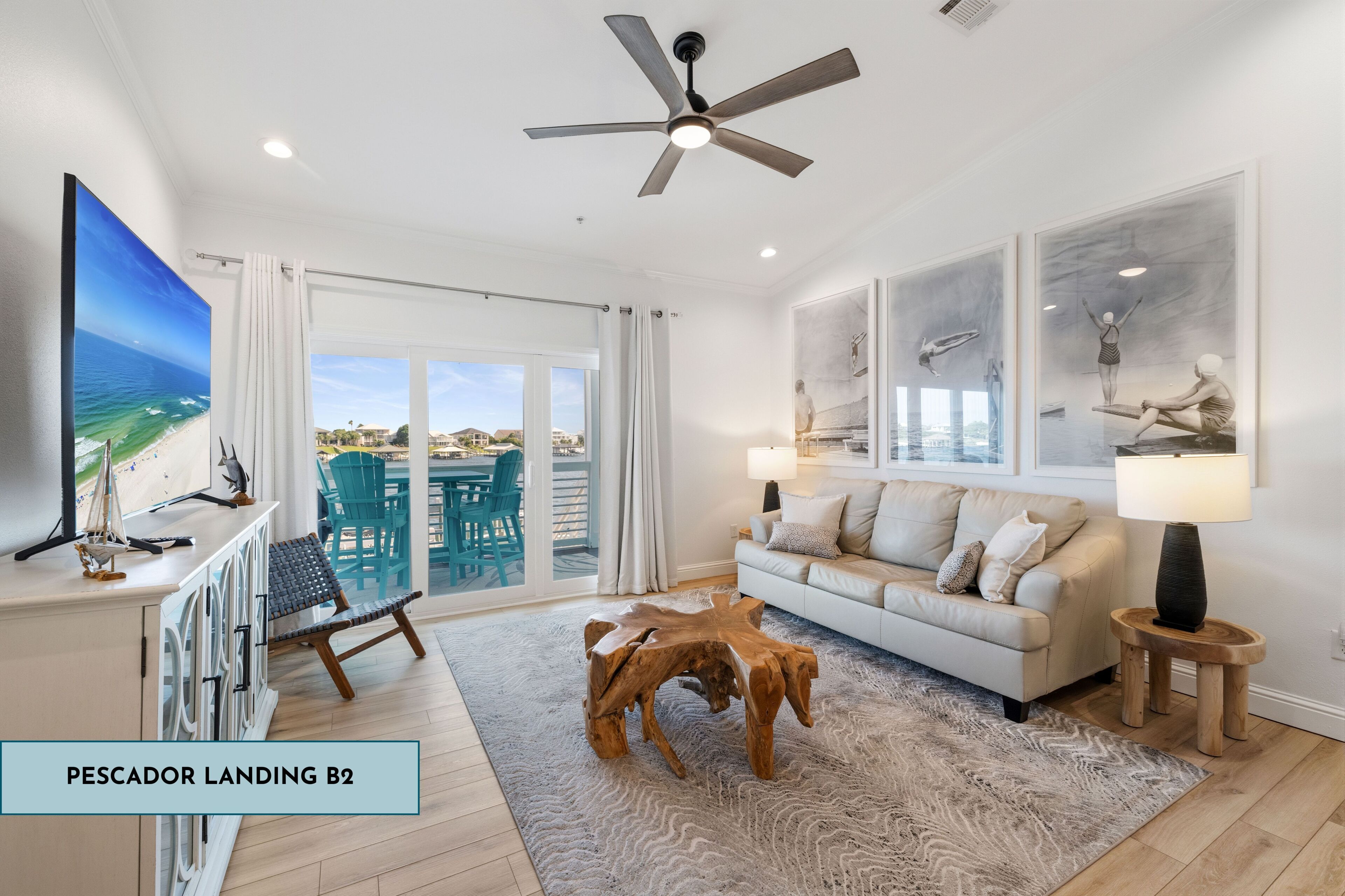 A spacious living room with a large window, a ceiling fan, a wooden coffee table, and a sofa with a view of the ocean.