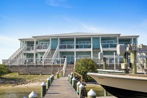 Un immeuble à plusieurs étages, avec un quai menant à un bateau, entouré d’une terrasse en bois et de bornes d’amarrage.