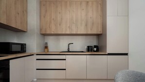 Una cocina moderna con armarios de madera, un microondas negro, un lavamanos y una tetera.