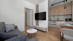 Una sala de estar moderna con un sofá gris, una mesita blanca y un televisor montado en la pared.