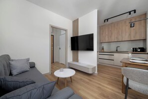 Un soggiorno moderno con un divano grigio, un piccolo tavolino bianco e un televisore montato a parete.