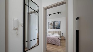 Un pasillo que conduce a un dormitorio con cama, mesita de noche y una lámpara fijada a la pared.