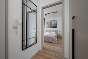 Un corridoio che conduce a una camera da letto con un letto, un comodino e un punto luce a parete.