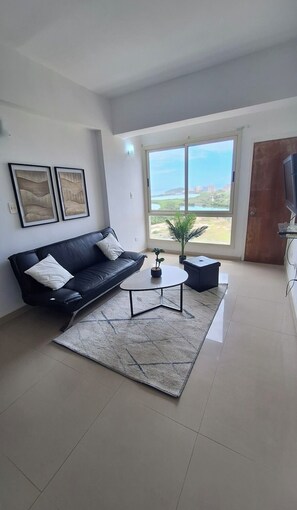 Una sala de estar con un sofá de cuero negro, una mesa de centro, una planta en maceta y un ventanal con vistas al exterior.