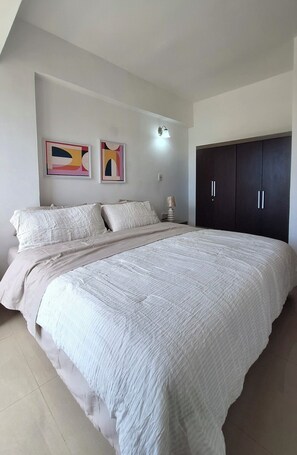 A bedroom with a large bed, two wall-mounted artworks, a bedside lamp, and a dark wardrobe. - Ideal apartment for your vacations in Margarita Island (Nueva Esparta)