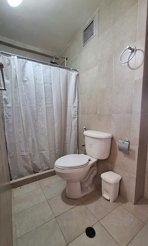 A bathroom with a toilet, a small trash bin, a shower curtain, and a toilet paper holder. - Ideal apartment for your vacations in Margarita Island (Nueva Esparta)