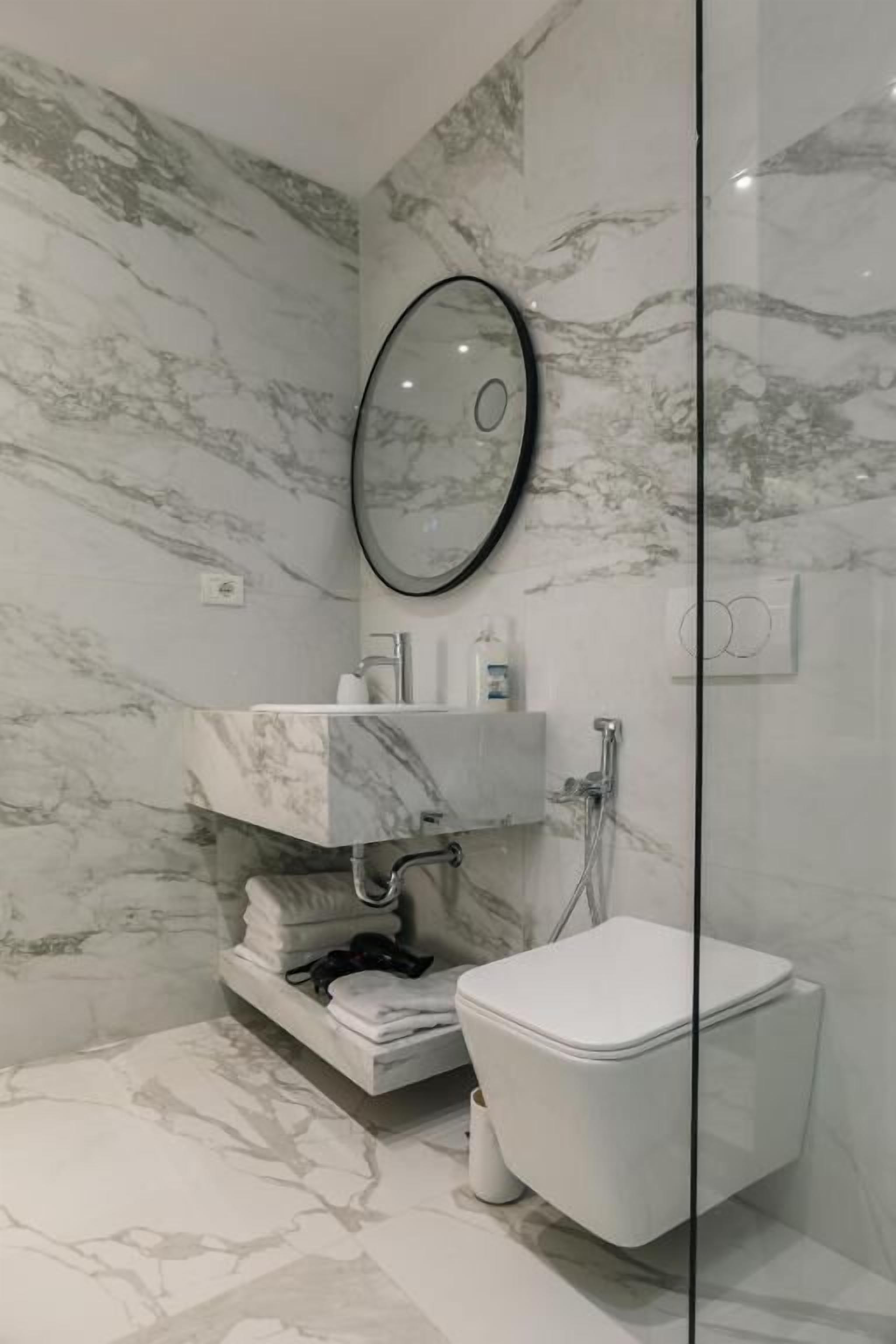 A bathroom with a marble wall, a white toilet, a glass shower enclosure, and a mirror.