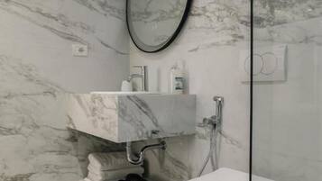 A bathroom with a marble wall, a white toilet, a glass shower enclosure, and a mirror.