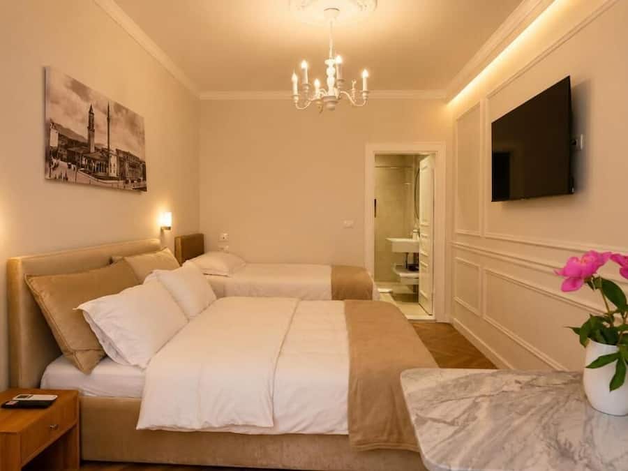 Habitación de hotel con dos camas, un candelabro, un televisor de pantalla plana, un cuadro y un jarrón con flores.