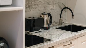 A kitchen with a black induction cooktop, a stainless steel kettle, a black toaster, and a black faucet.