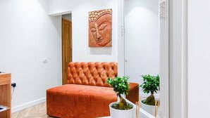 A bedroom with a tufted orange sofa, a wooden door, a wall-mounted artwork, and two potted plants.