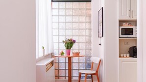 Una pequeña cocina con ventana, una mesa con una silla y armarios blancos.