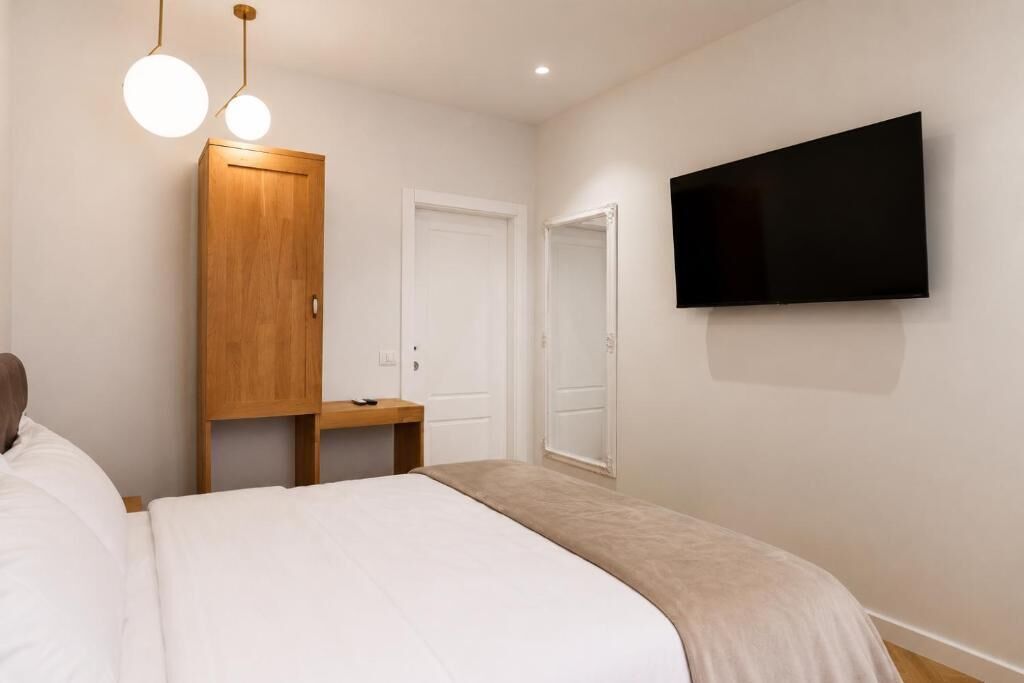 Une chambre à coucher comprenant un lit, une armoire en bois, un téléviseur fixé au mur et une table de chevet.