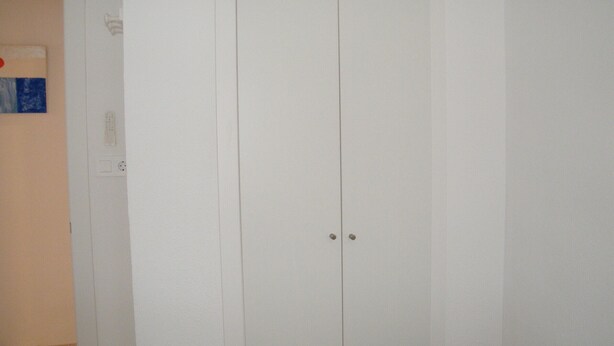 A white wardrobe with two doors, a light switch, and a power outlet on the wall. - Family apartment, sea view, parking - 7 guests (Gandia)
