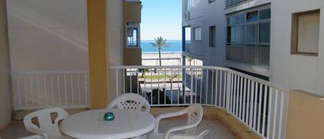 A balcony with a white table and chairs, overlooking a beach and buildings.
