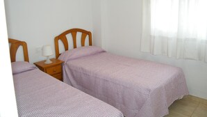 A bedroom with two single beds, a nightstand with a lamp, and a window with sheer curtains. - Family apartment, sea view, parking - 7 guests (Gandia)