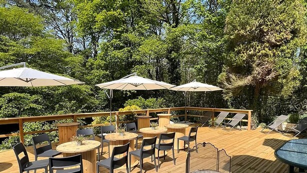 Une terrasse extérieure avec des tables et des chaises rondes, des parasols et un foyer.