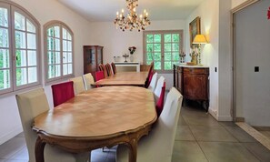 A dining room with a large wooden table, chairs, a chandelier, and large windows. - Spacious and peaceful villa - 15 guests (HERBEVILLE)