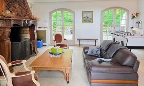 A living room with a fireplace, a wooden coffee table, a leather sofa, and a foosball table. - Spacious and peaceful villa - 15 guests (HERBEVILLE)