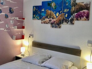 Ein Hotelzimmer mit Bett, Nachttischen, einer Wand mit maritimer Kunst und einer Steckdose.
