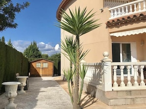 Ein Gebäude mit Holzbau im Hintergrund, einem weißen Balkon mit filigraner Brüstung und einer Palme im Vordergrund.