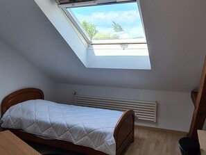 Una habitación pequeña con cama individual, tragaluz, radiador y cabecera de madera.
