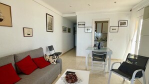 A living room with a sofa, coffee table, and chairs. There is a dining area with a table and chairs. The room has framed pictures on the walls.