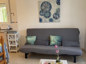 Ein Wohnzimmer mit grauem Sofa, zwei Kissen, einem kleinen weißen Beistelltisch, einer Topf-Orchidee und einem an der Wand hängenden abstrakten Gemälde.