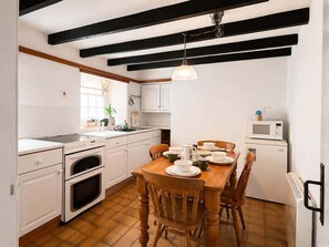 A kitchen with white cabinets, a wooden dining table, and a white refrigerator. - Heart of St Davids Cottage| Parking | Pet Friendly (St Davids)