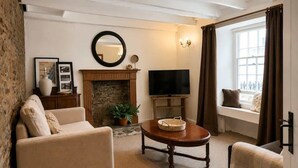 Ein Wohnzimmer mit Kamin, Fernseher, einer Couch und einem Fenster mit Vorhängen.